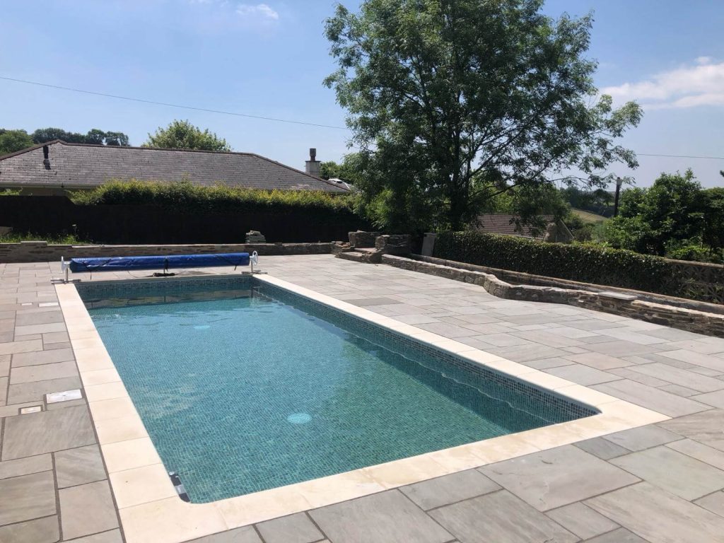 Open outdoor pool with teal tiling. The pool is rectangular and has an outdoor patio surrounding it. 