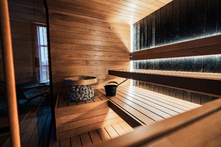Experience relaxation in a contemporary wooden Finnish sauna. Features a large stone heater, multi-level seating, and subtle LED lighting for ambient luxury.