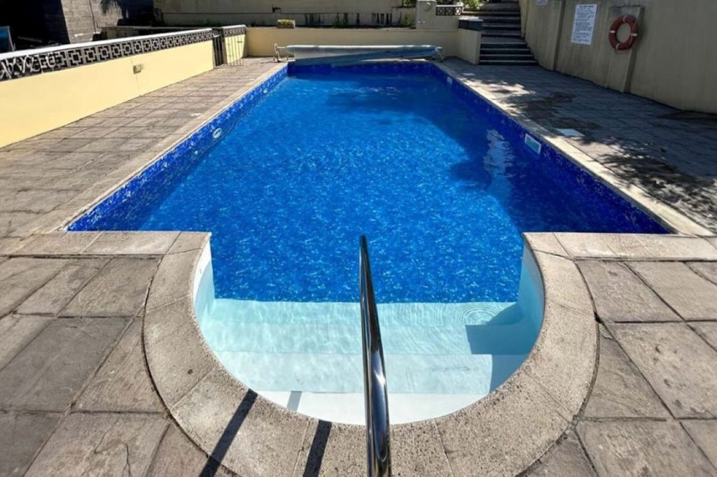 Discover a beautiful outdoor swimming pool with bright blue water, curved entry steps, and a shiny handrail, surrounded by stone paving